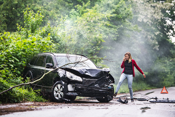 An angry and frustrated young woman with smartphone by the damaged car after a car accident, making a phone call. Copy space.