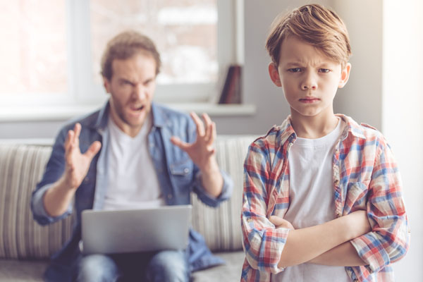 Sad little boy is looking at camera while his father is yelling at him in the background